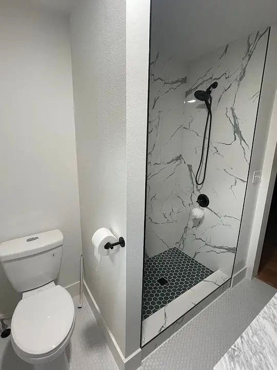 Modern bathroom featuring a glass shower and sleek fixtures, with marble walls and hexagon tiles.