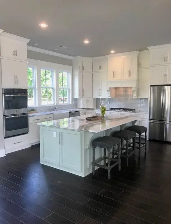 Modern kitchen with white cabinets, granite island, stainless steel appliances, and hardwood floors.