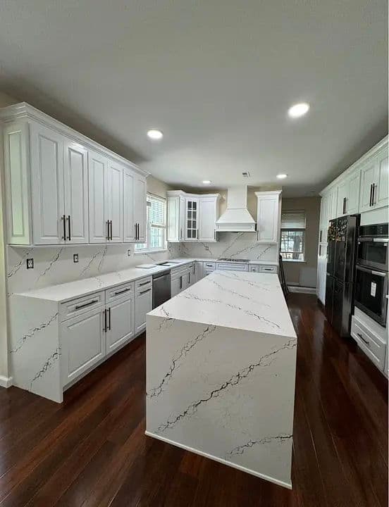 Modern kitchen with white cabinets, marble countertops, and hardwood flooring. Spacious layout.