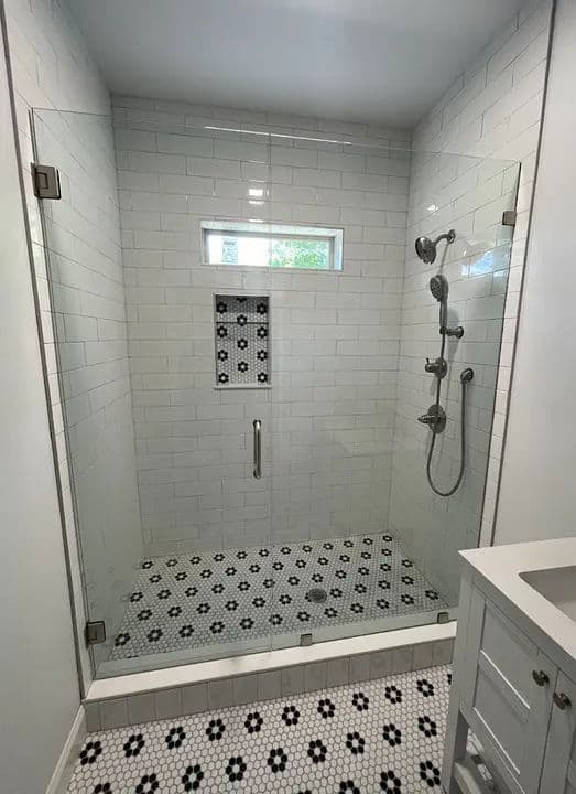 Modern glass shower with white subway tiles and black hexagonal floor, featuring dual showerheads.