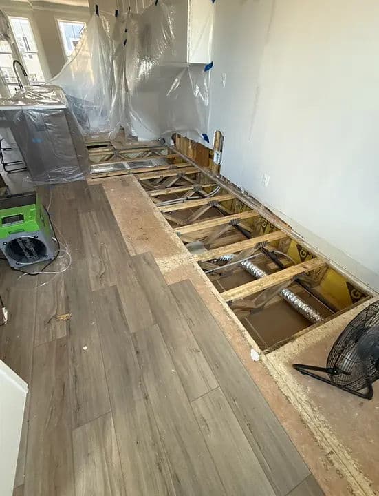 Exposed flooring and renovations in a home with protective coverings and fans installed.