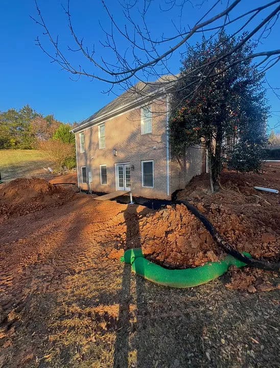 House undergoing landscaping with drainage pipe in yard and bare soil around foundation.