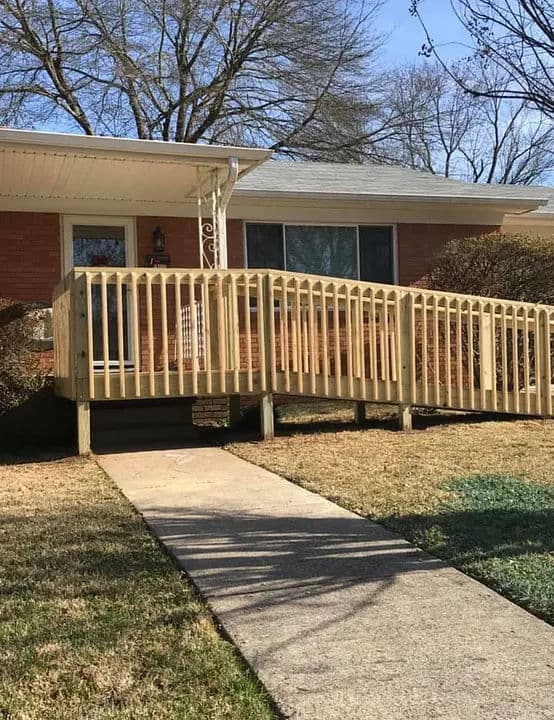 Accessible home with wooden ramp and pathway, featuring a brick exterior and landscaped yard.