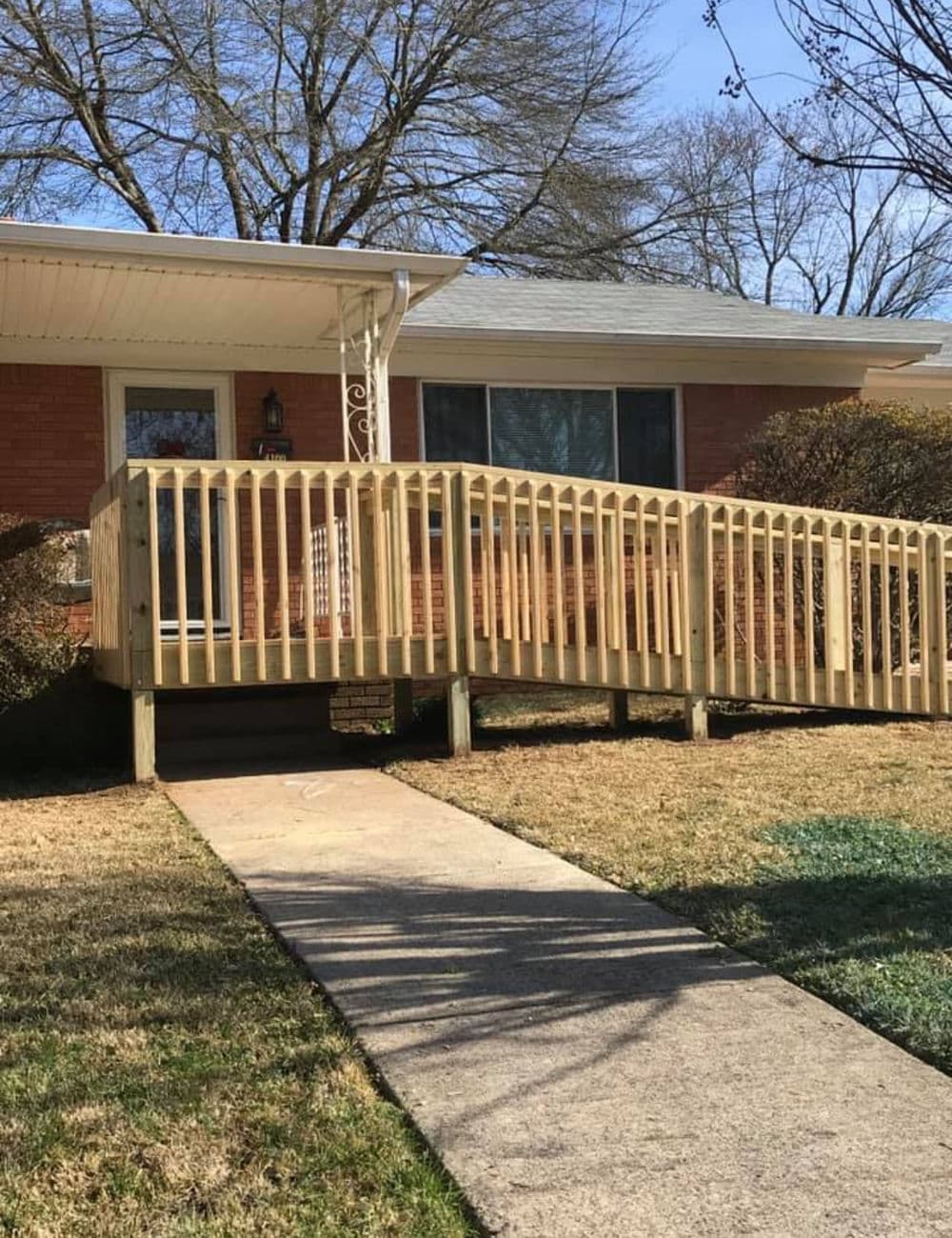 Accessibility ramp leading to a brick house, surrounded by grass and trees on a sunny day.