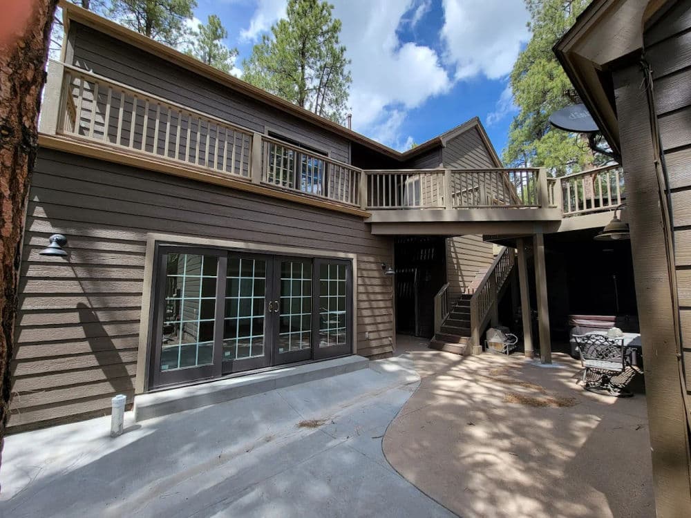 Spacious outdoor area of a modern cabin with stairs, deck, and surrounded by pine trees.