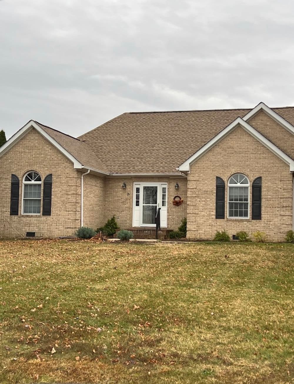 Brick house with a sloping roof, front porch, and landscaped yard on a cloudy day.